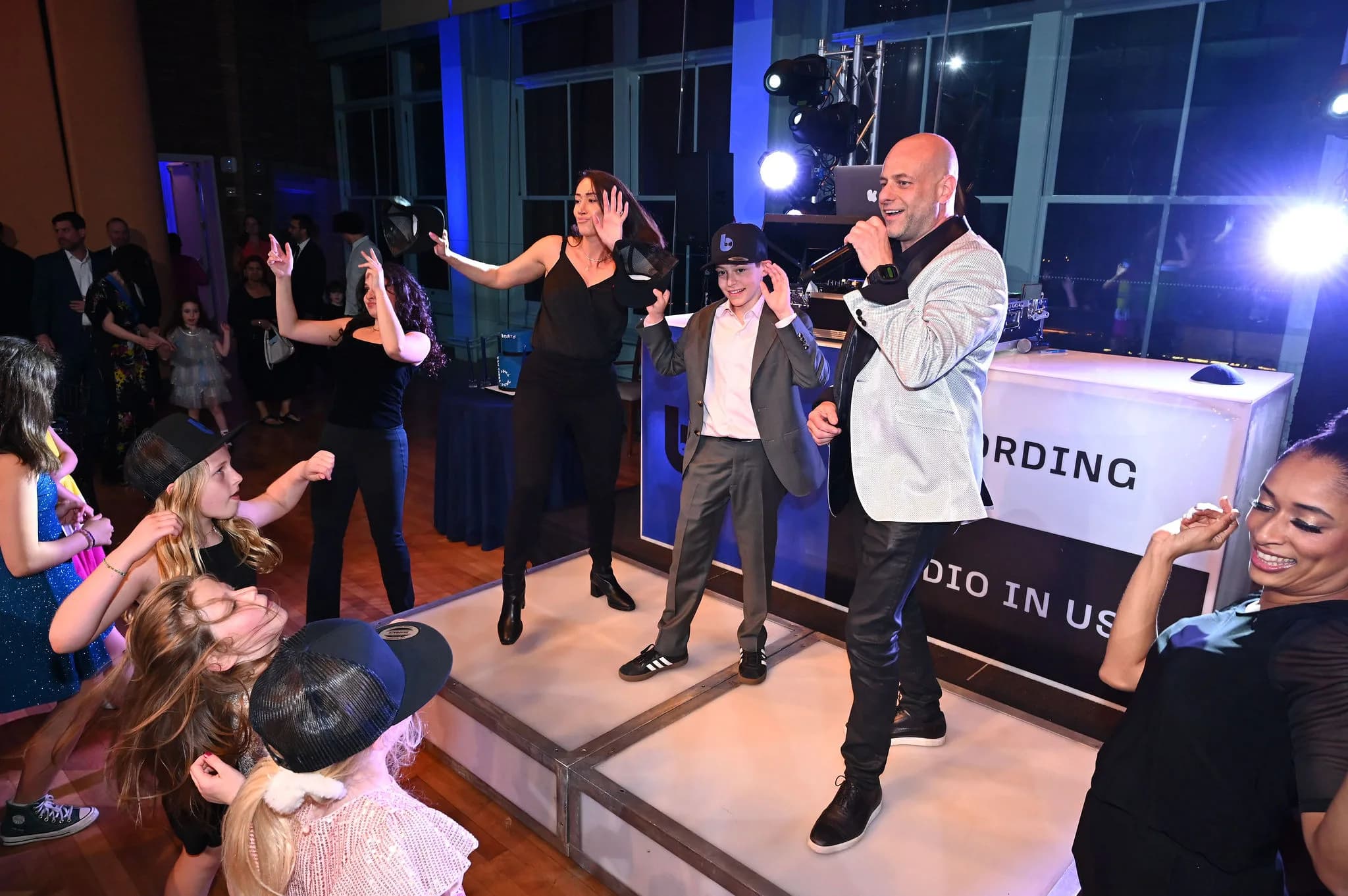 High-energy bar mitzvah with the MC and dancers on a lit stage and a crowd of kids celebrating